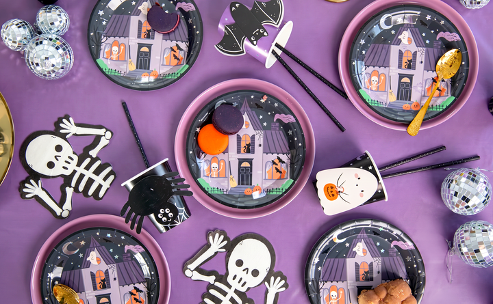 Halloween Spooky Friends servetter med skelett på ett dukat Halloweenbord tillsammans med tallrikar och muggar.